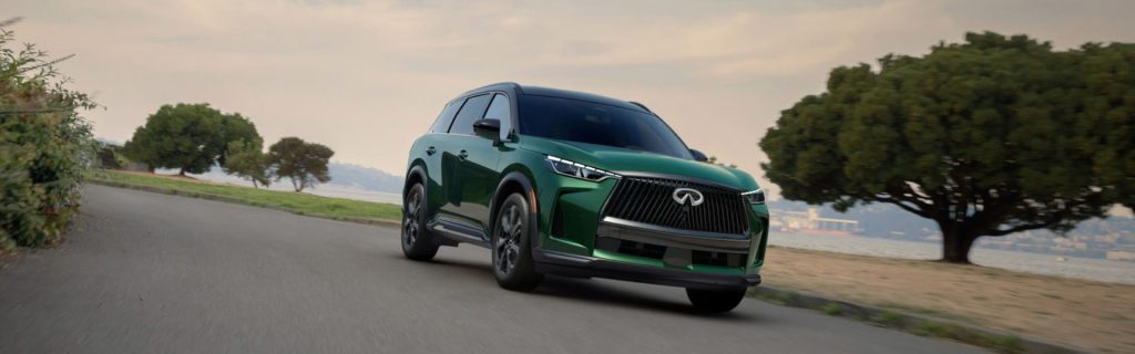 Green Infiniti QX60 driving on a coastal road.